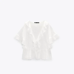 Vit blus med volangdetaljer - Supersnygg vit blus från Zara med volangdetaljer längs kanterna. Endast använd ett fåtal gånger så superbra skick! Skriv för fler bilder