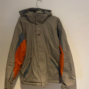 Grå jacka från Helly Hansen - Säljer en grå jacka från Helly Hansen med orange och mörkgrå detaljer. 