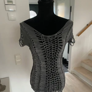 Grå klänning med snörning - Snygg grå klänning med unik snörningsdetalj framtill och på ärmarna. Den har en tight passform och är tillverkad i ett stretchigt material som framhäver figuren. Perfekt för en kväll ute eller en speciell tillställning.