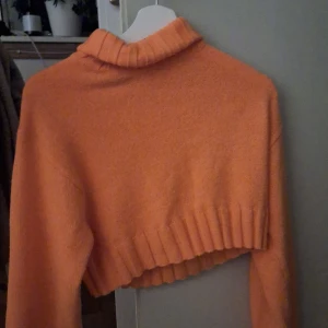 Orange croppad polotröja - Säljer en snygg orange croppad polotröja med ribbad nederkant. Perfekt för en trendig look i höst och vår. Tröjan har långa ärmar och en mysig polokrage.