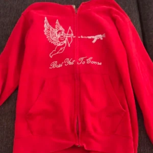 Röd huvtröja med tryck - Snygg röd huvtröja med dragkedja och ett unikt tryck av en ängel och texten 'Best Yet To Come'. Perfekt för en avslappnad stil. Lånade bilder av förra ägaren, köpt på plick innan 