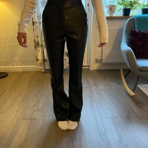 Svarta skinnbyxor från Madlady - Snygga svarta skinnbyxor från Madlady med hög midja och bootcut-stil. Perfekta för en trendig look, dessa byxor har en smickrande passform och är tillverkade i ett syntetiskt material som ger en cool läderkänsla.