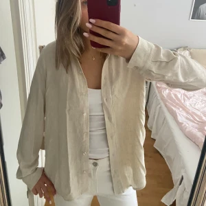 Beige linneskjorta från Selected Femme - Säljer en stilren beige skjorta från Selected Femme i storlek S. Skjortan har långa ärmar och knappar framtill, perfekt för en avslappnad look. Tillverkad i ett mjukt material som ger en skön känsla. Använt ett fåtal gånger men den är i bra skick, en liten sminkfläck på insidan vid lappen som inte syns. Perfekt på våren eller på sommaren över bikinin. 