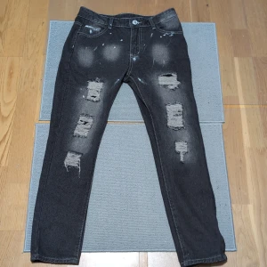 Svarta jeans med slitningar - Coola svarta jeans med slitningar och blekta detaljer. Perfekta för en avslappnad stil. Tillverkade i en bomulls- och polyesterblandning för komfort och hållbarhet.