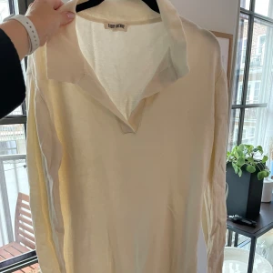 Krämfärgad klänning från Djerf Avenue - Säljer en stilren krämfärgad klänning från Djerf Avenue. Klänningen har en klassisk krage och långa ärmar, perfekt för en elegant look. Den är i en mjuk och bekväm kvalitet.