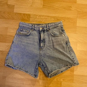 Blå jeansshorts från Gina Tricot - Säljer ett par klassiska blå jeansshorts från Perfect Jeans. De har en högmidjad passform med fyra fickor och knappgylf. Perfekta för sommaren!