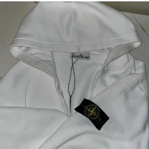 Vit hoodie från Stone Island - Säljer en stilren vit hoodie från Stone Island med dragkedja och den ikoniska loggan på ärmen. Perfekt för en avslappnad och trendig look. Pris kan diskuteras 