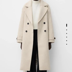 Beige kappa med knappar - Elegant beige kappa med dubbelknäppning. Kappan har långa ärmar och dekorativa knappar vid ärmsluten. Nästintill oanvänd  