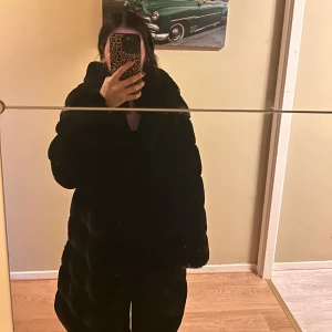 Svart pälsjacka med luva  - Svart pälsjacka med luva i mycket fint skick! Jackan har knappar som man stänger med. Storlek S