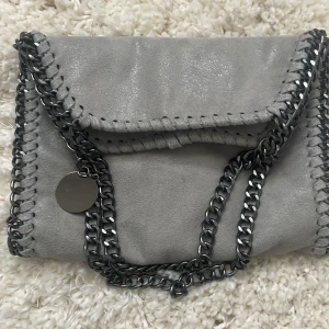 Stella Mcartney likande väska - Snygg grå väska i mocka med en glittrig finish. Väskan är  använd en gång och har en liten fläck på baksidan som inte syns när man har på sig den💝