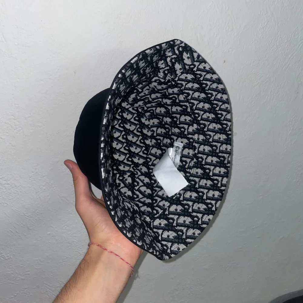 Snygg svart bucket hat från Christian Dior med ett unikt mönster på insidan. Hatten har små ventilationshål på sidorna för extra komfort. Perfekt för att ge din outfit en stilfull touch. Pris kan diskuteras vid snabb affär!!!. Asusteet.