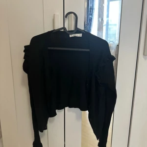 Svart kofta från Zara - Säljer en stilren svart kofta från Zara Knit. Koftan har långa ärmar och en croppad design som ger en modern look. Perfekt för lager-på-lager-stil eller som ett lättare ytterplagg.