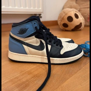 Nike Air Jordan 1 obsidian  - Snygga Nike Air Jordans i en stilren kombination av blått, vitt och svart. Skorna har klassisk snörning och en hög siluett som ger ett sportigt intryck. Perfekta för dig som vill ha en ikonisk sneaker med tidlös design. Nästan aldrig använd och i helt ny skick. Skicka för fler bilder! Köpta för 5000 