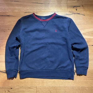 Mörkblå tröja från Polo Ralph Lauren - Pris kan sänkas, Säljer en mörkblå tröja från Polo Ralph Lauren med röda detaljer, den är perfekt för personer som är ungefär 160cm men den kan gå upp till 170cm. Vid mer frågor skicka ett dm.