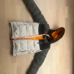 Svart/grön skidjacka från Brunotti, 152 cm  - Säljer en snygg pufferjacka / skidjacka  från Brunotti i grått och grönt/svart med orange foder. Jackan har en dragkedja framtill samt liftkortshållare. Jackan har snölås. Modellen heter Sanclairy Boys Puffer Snow. 152 cm  