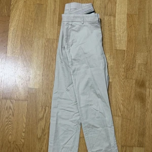 Byxor  - Säljer två par chinos, ett i beige och ett i mörkblått. De har en klassisk design med dragkedja och knappar. Perfekta för en stilren look. Det kostar 50kr st.