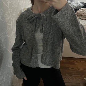 Grå kofta med knytband - Säljer en mysig grå kofta med knytband framtill. Snyggt att även använda den som en tröja och ha knytningen bak vid ryggen. Aldrig använd!🤗