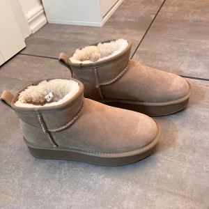 Beige mocka boots med foder - Säljer ett par bekväma beige boots i mocka med mjukt foder. Perfekta för kyliga dagar med sin varma insida och stilrena design. De har en låg klack och en praktisk dragflik baktill. Använda endast 1 gång. Nypris 749. OBS: ”fläckarna” är inte smuts utan mocka fläckar. 