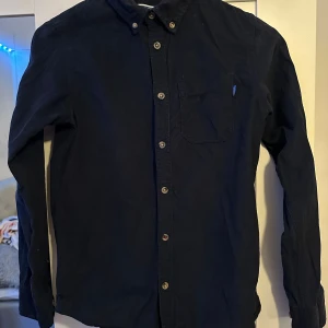 Mörkblå skjorta från Jack & Jones - Snygg mörkblå skjorta från Jack & Jones med långa ärmar och klassisk krage. Skjortan har knappar framtill och en bröstficka. Perfekt för en stilren look.