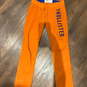 Orange mjukisbyxor från Hollister - Säljer ett par orange mjukisbyxor från Hollister med blå logga längs benet. Färgen är lite mörkare i verkligheten. Har några fläckar men de går nog bort i tvätten 