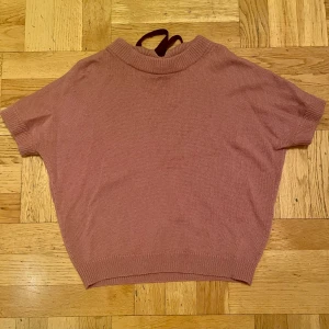 Rosa tröja från Massimo Dutti - Säljer en mjuk rosa tröja från Massimo Dutti i ull och kashmir. Tröjan har korta ärmar och en dekorativ knytning i halsen. Perfekt för en stilren och bekväm look.