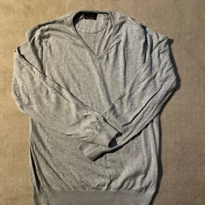 Grå v-ringad tröja från Massimo Dutti - Säljer en stilren grå v-ringad tröja från Massimo Dutti. Tröjan är tillverkad i en mjuk blandning av bomull och kashmir, vilket gör den både bekväm och elegant. Perfekt för kyligare dagar.