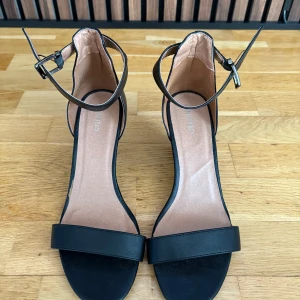 Svarta kilklackssandaler med ankelrem - Snygga svarta sandaler med kilklack och justerbar ankelrem från Anna Field. Perfekta för en stilren look med öppen tå och bekväm passform. Aldrig använda. 