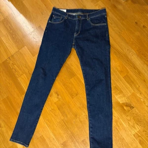 Mörkblå jeans från J.Lindeberg - Snygga mörkblå jeans från J.Lindeberg med klassisk femficksdesign och guldfärgade sömmar. Perfekt för en stilren look. De har en knappgylf och är tillverkade i ett slitstarkt denimtyg.