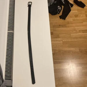 Svart bälte med silverfärgat spänne - Snyggt svart bälte med ett klassiskt silverfärgat spänne. Perfekt för att ge en stilren touch till din outfit. Bältet har flera hål för justerbar passform. Ett bra skick men säljs billigt