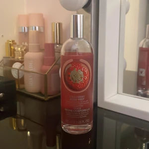 Strawberry Mist Body Spray - Fräsch och fruktig kroppsspray med jordgubbsdoft. Kommer i en genomskinlig flaska med röd etikett och silverfärgad spraykork. Perfekt för en uppfriskande känsla under dagen.