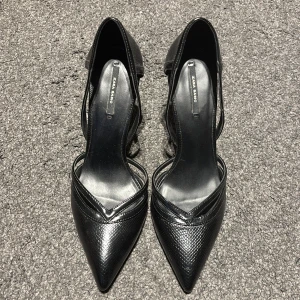Svarta pumps från Zara - Eleganta svarta pumps från Zara med spetsig tå och hög klack. Skorna har en stilren design med texturerat material som ger en lyxig känsla. Perfekta för en kväll ute eller en formell tillställning. Stor i stl. 