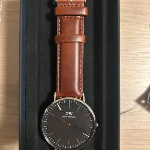 Klocka från Daniel Wellington med brunt läderarmband - Snygg klocka från Daniel Wellington med ett stilrent brunt läderarmband och svart urtavla. Aldrig använt
