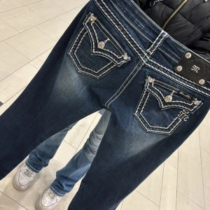 Blå jeans från Miss Me - Snygga blå jeans från Miss Me med dekorativa sömmar och detaljerade bakfickor. Jeansen har en slim-stil och är perfekta för en avslappnad look. De har en klassisk femficksdesign och knappar med mönster.