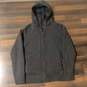 Grå stickad cardigan  - Säljer en grå stickad cardigan med luva Cardiganen har ribbade muddar och en normal passform, perfekt för kyliga dagar. Huvan är fodrad för extra värme. Storlek L (sitter mer som M). BVSA