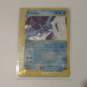 Articuno Pokémonkort - Säljer ett Articuno Pokémonkort med blå och gul design. Kortet har en bild av Articuno och text med dess förmågor och statistik. Perfekt för samlare eller Pokémonfans!