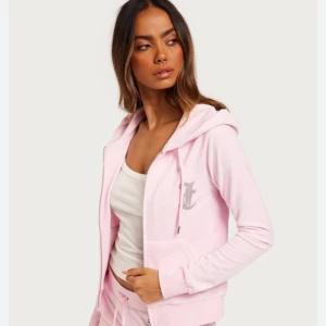 Rosa hoodie från Juicy Couture - Säljer en mjuk och bekväm rosa hoodie från Juicy Couture med dragkedja och huva. Den har ett glittrigt Juicy-tryck på ryggen och en liten logga på bröstet. Säljer då den knappt kommer till användning. Köpt för 1600kr.