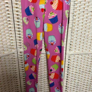 Färgglada leggings med cupcake-mönster - Snygga och lekfulla leggings i lila med ett färgglatt cupcake-mönster. Perfekta för dig som vill sticka ut och ha något unikt i garderoben. De är stretchiga och bekväma, vilket gör dem idealiska för en avslappnad stil.