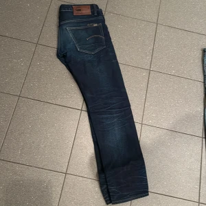 Mörkblå jeans från G-Star Raw - Snygga mörkblå jeans från G-Star Raw, modell 3301. De har en klassisk femficksdesign och en knappgylf. Perfekta för en stilren look. 