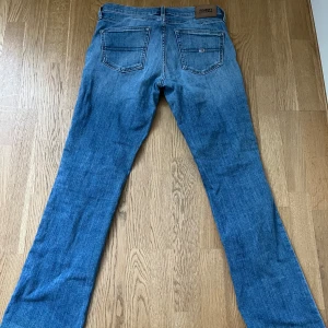 Blå bootcut jeans från Tommy Hilfiger - Snygga blå bootcut jeans från Tommy Hilfiger med klassisk femficksdesign. Jeansen har en lätt tvättad look och är perfekta för en avslappnad stil. De har en knapp- och dragkedjestängning framtill. Använda endast en gång💕