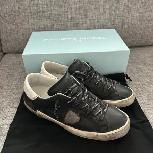 Svarta sneakers från Philippe Model - Snygga svarta sneakers från Philippe Model med vita detaljer och snörning. Skorna har en stilren design med märkets logga på sidan och en bekväm sula. Hör av er för mer info.