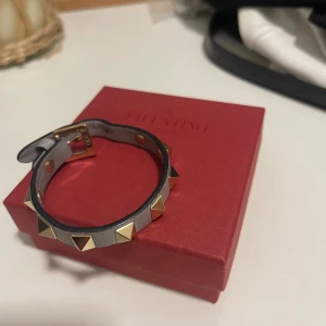 Grått armband med nitar från Valentino - Snyggt grått armband från Valentino med guldiga  nitar, modellen är ”rockstud”. Armbandet har ett justerbart spänne och kommer i originalbox. Kvitto finns! Medföljer tyvärr inte dustbag då jag tappat bort den men det finns extra nitar🪩🕺🏼🤘🏼den är varsamt använd så fortfarande i toppskick!