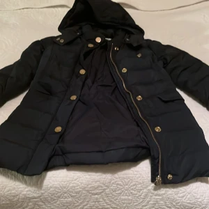  Marin blå dunjacka från Armani Junior - Snygg marin blå dunjacka från Armani Junior med huva och dragkedja. Jackan har knappar och är perfekt för kyliga dagar. Den quiltade designen ger extra värme och stil. Kommer i mycket gott skick rök och djur fritt. Och är för 106 cm.