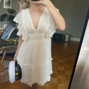 Vit klänning med spetsdetaljer. Studentklänning - Charmig vit klänning med v-ringning och spetsdetaljer. Klänningen har korta ärmar med volang och ett prickigt mönster. Otroliga detaljer och en så fin öppen rygg. Perfekt studentklänning. Köpt på nelly för ca800kr. Tycärr förliten för mig. 