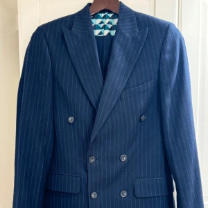 Dubbelknäppt mörkblå pinstripe kostym - Märke: Harry Brown Storlek Kavaj: 46 Storlek Byxor: 32/32 Passform: Slim fit Färg: Mörkblå med pinstripe Skick: Mycket bra (nästan ny) Detaljer: Dubbla knappar fram, mönstrat innerfoder