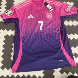 Rosa och lila fotbollströja  - Snygg fotbollströja från Adidas i rosa och lila med nummer 7 och namntryck på ryggen. Tröjan har korta ärmar och ett coolt mönster framtill. Perfekt för fotbollsfans!