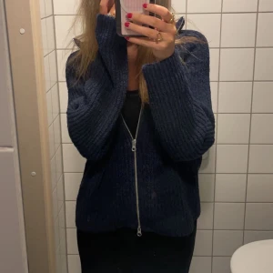 Mörkblå stickad kofta med dragkedja - Säljer en mysig mörkblå stickad kofta med dragkedja framtill. Koftan har långa ärmar och en bekväm passform.