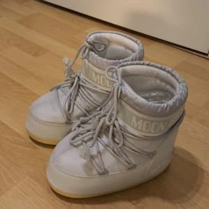 Grå Moon Boots med snörning - Snygga och trendiga grå Moon Boots med snörning och en robust sula. Perfekta för kalla vinterdagar med sin varma och bekväma design. De har en stilren look med logotypdetaljer på sidan och baksidan.           Knappt använda. Köptes i mars 2024 och har använts max 10 gånger sen dess.  De är superfina men tyvärr har jag ångrat mig och känner att det inte riktigt är min stil.  Storlek 39-41.