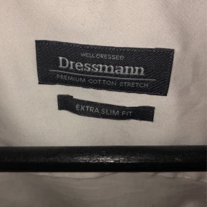 Vit skjorta från Dressmann - Säljer en stilren vit skjorta från Dressmann i extra slim fit. Skjortan är gjord av premium bomull med stretch för en bekväm passform. Den har långa ärmar och knappar hela vägen ner. Passar perfekt till både kostym och jeans. Inga fläckar, snålanvänd