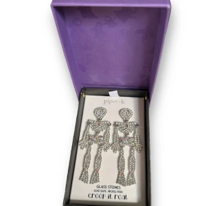 Glittriga skelettörhängen från Piper K - Supercoola och unika skelettörhängen från Piper K! De är gjorda av glittriga glasstenar och är både bly- och nickelfria. Perfekta för Halloween eller när du vill sticka ut lite extra. Kommer i en söt lila förpackning med spöken på. 🖤