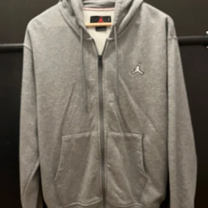 Grå hoodie från Jordan - Säljer en grå hoodie från Jordan i storlek M. Den har en dragkedja framtill och är långärmad med en klassisk Jordan-logga på bröstet. Insidan är fodrad med mjuk fleece för extra komfort. Perfekt för höst och vår!